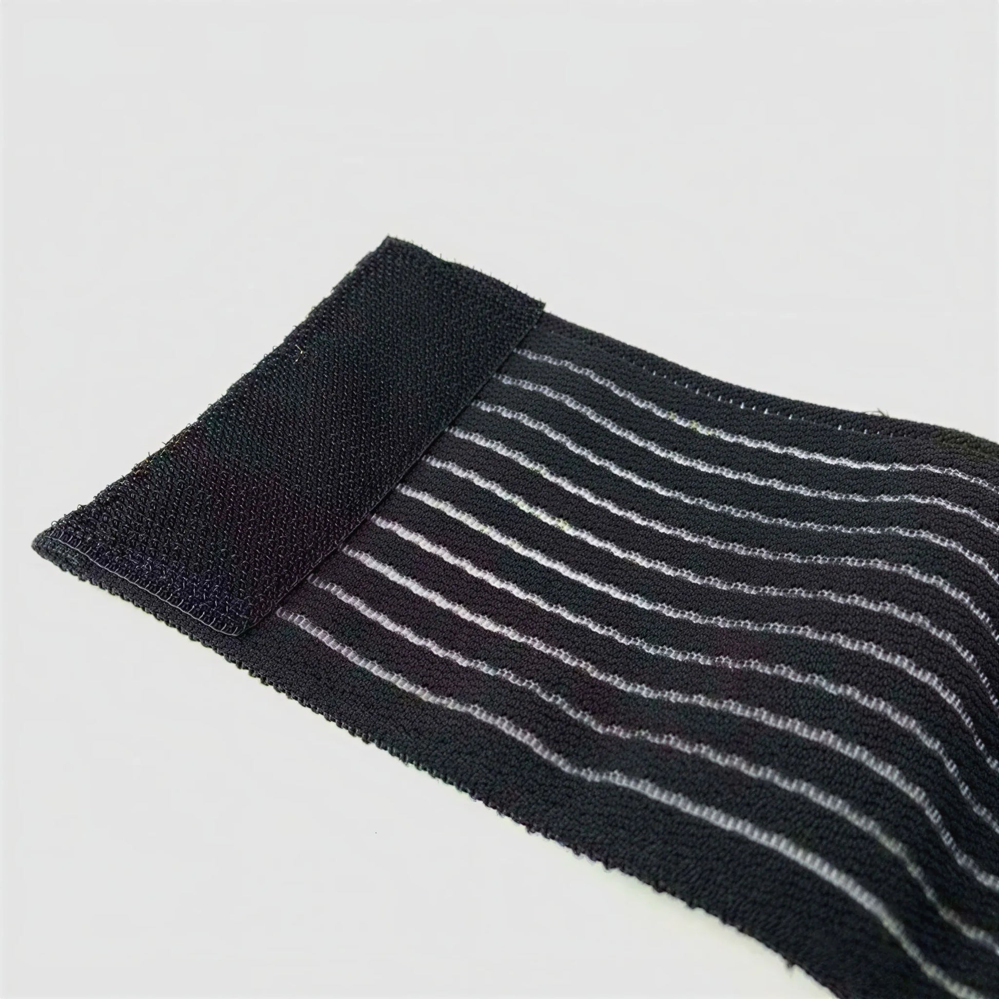 Närbild av elastiskt fotledsband i svart och grått med randig, följsam materialstruktur.